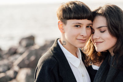 Lesbian women embracing while standing on rock against sea