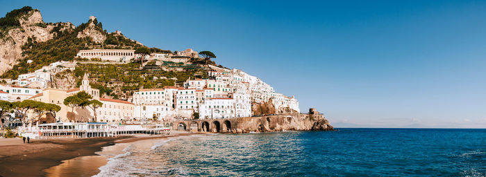 Buildings by sea against clear blue sky