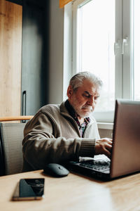 An elderly man works at a laptop, learning from home, home bookkeeping