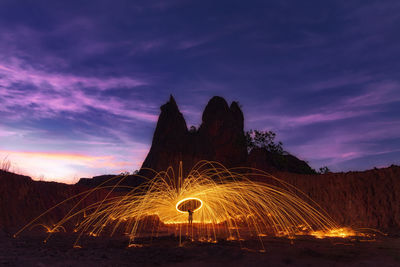 Silhouette people by illuminated fire against sky at night