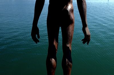 Midsection of naked man standing by sea