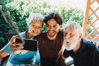 Smiling male caretaker taking selfie with senior man and woman at back yard