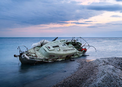 Abandoned ship on beach against sky during sunset