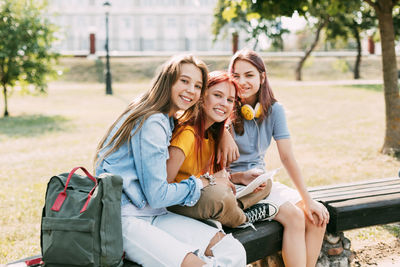 Three schoolgirls are sitting on a park bench, talking, preparing together with the lesson. 