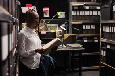 Rear view of woman using digital tablet while standing in library