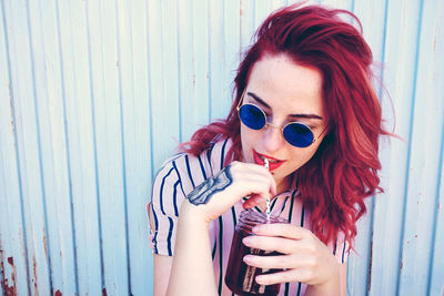 Woman having drink while sitting by wall