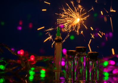 Close-up of syringe against sparklers in darkroom