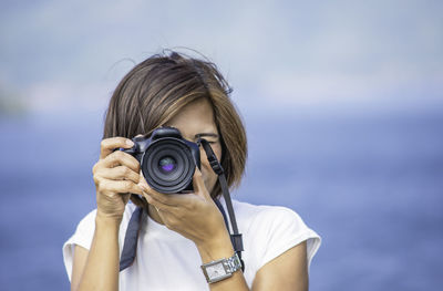 Woman photographing with digital camera against sea