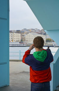 Rear view of boy standing against sky in city