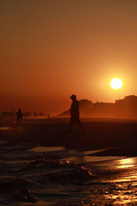 Silhouette man walking at beach against clear orange sky during sunset