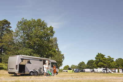 Family arranging chairs by camper van at trailer park against sky