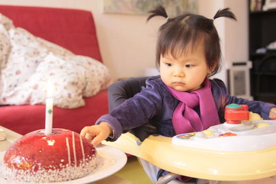 Cute girl sitting in baby walker by cake