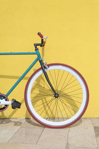 Bicycle parked against yellow wall at sidewalk in city