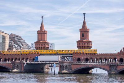 Bridge over river in city against cloudy sky