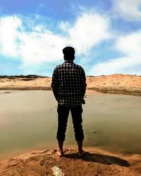 Rear view of man standing on shore against sky