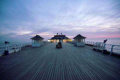 Lifeguard hut on pier by sea against sky at sunrise