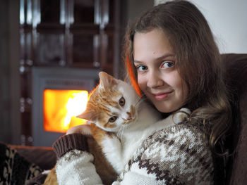Close-up portrait of smiling girl holding cat while sitting at home