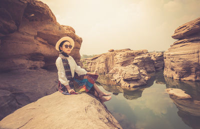 Man sitting on rock against sky