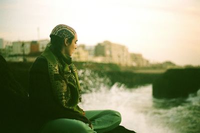 Woman sitting by river against sky
