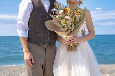 Midsection of woman standing by sea against sky