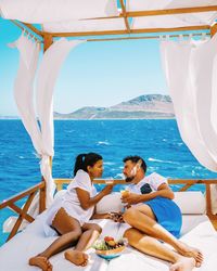 Couple talking while relaxing on bed in boat against clear sky