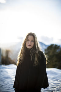 Portrait of young woman standing on snow against sky