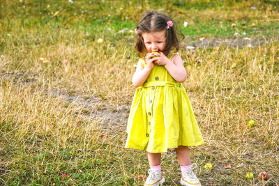 Little girl staying on meadow and eating green apple. kid playing outdoor in garden. cute