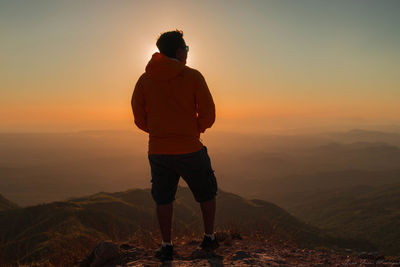 Rear view of man standing on mountain against orange sky