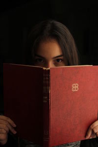 Portrait of young woman reading book against black background