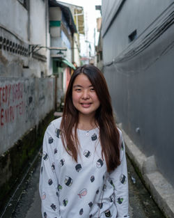 Portrait of smiling young woman standing in alley