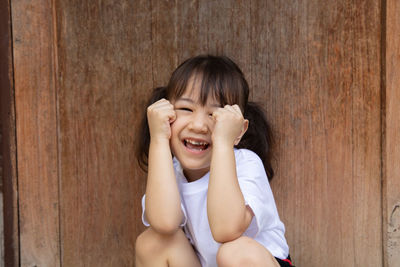 Portrait of cute girl smiling against wooden wall