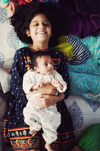 Portrait of happy girl with cute sister lying on bed at home