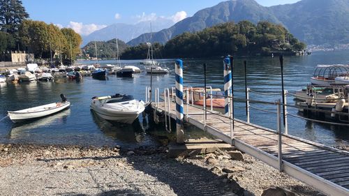 Boats moored at harbor by lake against sky