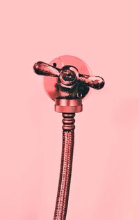 Low angle view of faucet and pipe against pink background