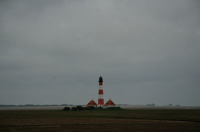 Lighthouse on field by building against sky