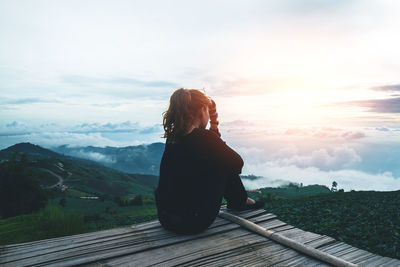 Rear view of woman sitting on mountain against sky