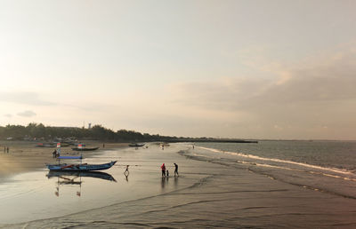 People on beach against sky during sunset