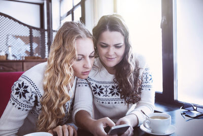 Women in sweater using smart phone at cafe