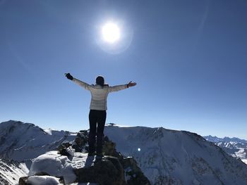 Low angle view of man standing on snowcapped mountain against clear sky