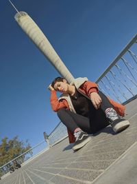 Low angle view of man with umbrella against clear blue sky