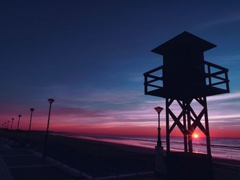 Silhouette lifeguard hut at beach against sky during sunset