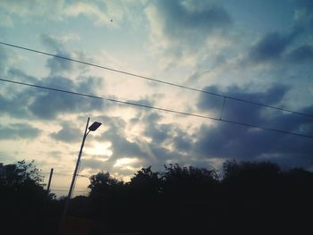 Low angle view of power lines against cloudy sky