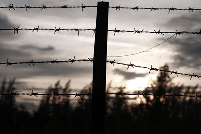 Close-up of silhouette barbed wire fence against sky