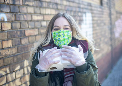 Portrait of woman holding mask against wall