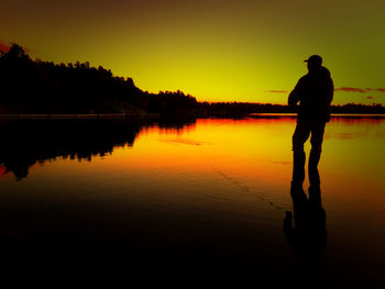 Silhouette of people standing in lake at sunset