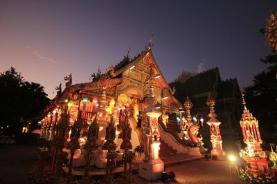 Illuminated temple by building against sky at night