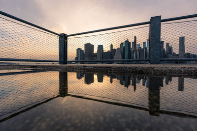 Reflection of buildings in city against sky during sunset