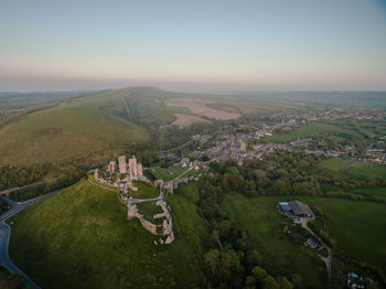 An aerial view of corfe castle in dorset with the sun rising over the sea in the background.