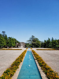 Road amidst field against clear blue sky