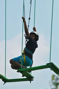 Low angle view of boy zip lining against sky